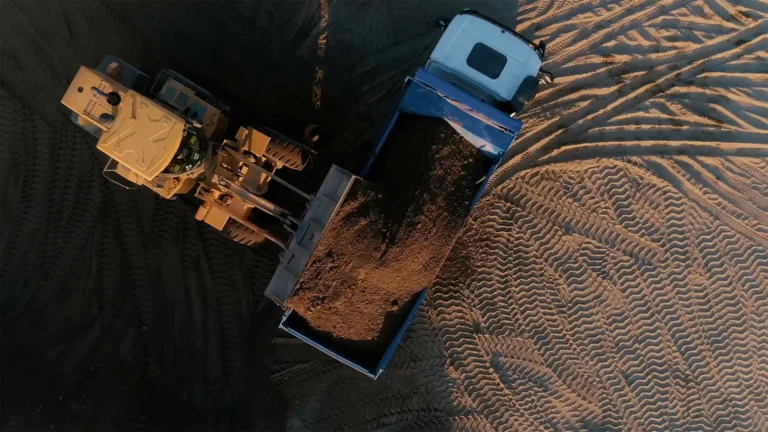 Aerial view of a front-end loader dumping soil into a mining truck at an open-pit mining site.